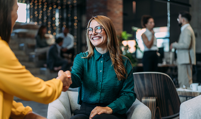 Woman wearing a long sleeved, dark green shirt shaking hands with another woman in a yellow shirt