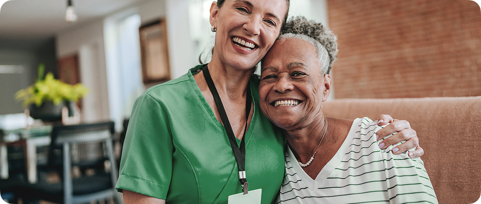 A nurse and her older patient smiling and hugging