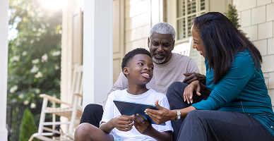 A family sitting on a porch together looking at a tablet