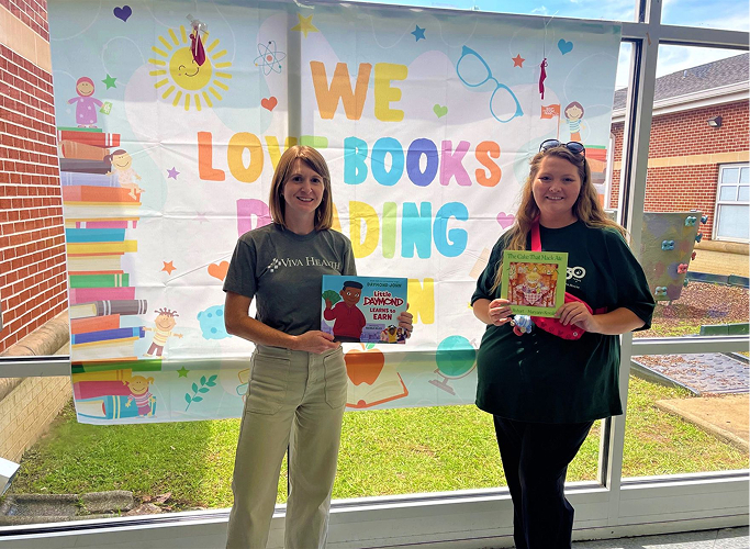 Two volunteers standing in a classroom reading books to young students.