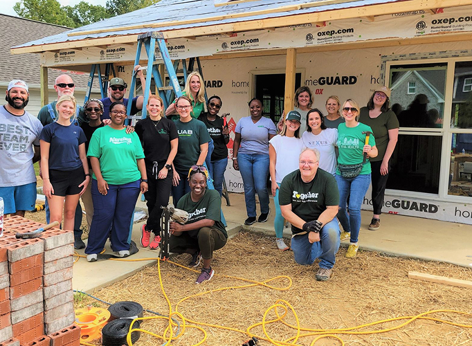 A large group of volunteers smiling in front of a partially constructed house.