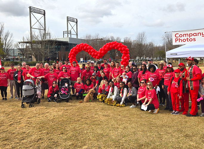 A large group wearing red shirts gathered behind a balloon heart at an outdoor event.