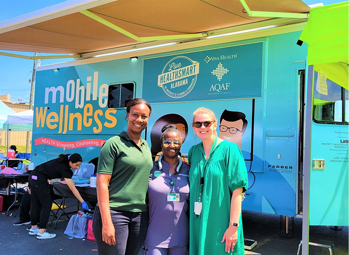 Three women posing outside in front of a bright blue Mobile Wellness clinic bus.