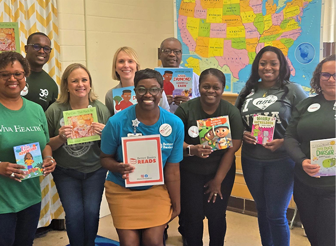 A group of volunteers smiling and holding up various children's books.