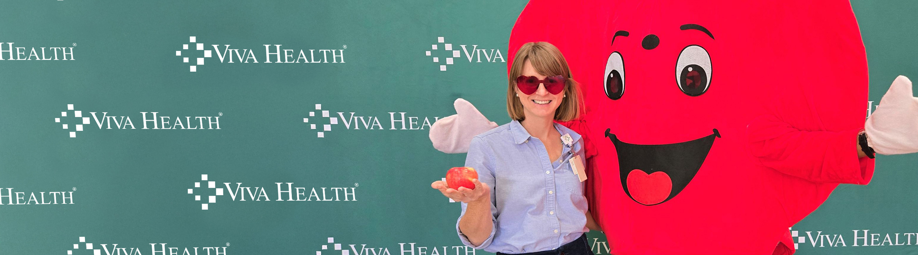 A woman and a heart mascot side hugging and waving