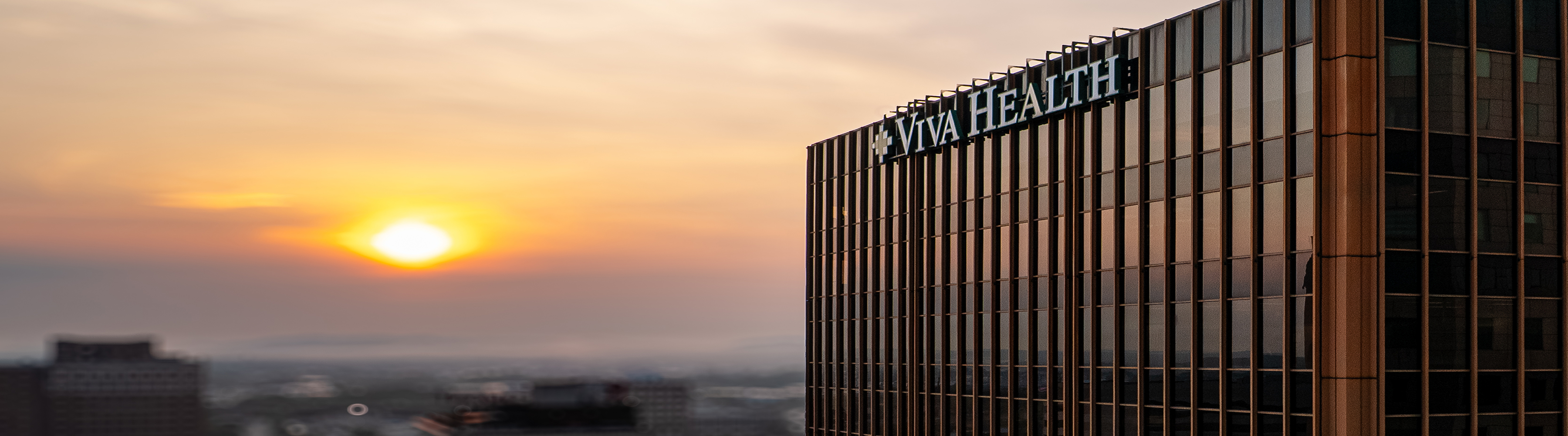 The Viva Health office building at sunset, with the Viva Health sign on its facade overlooking the city skyline