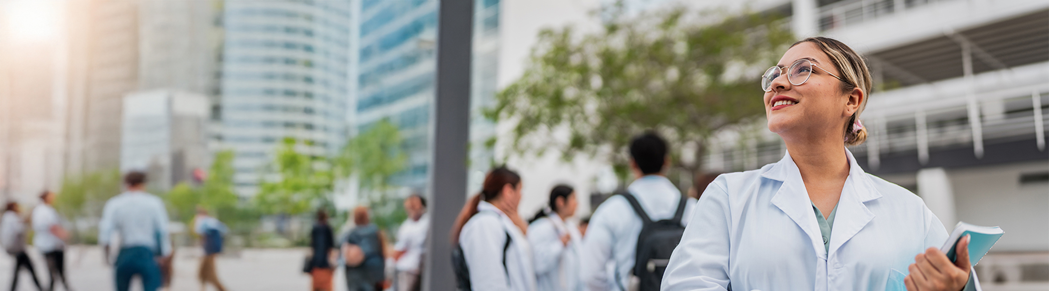 A medical student walking outside with a notebook in her hand, looking at the sky