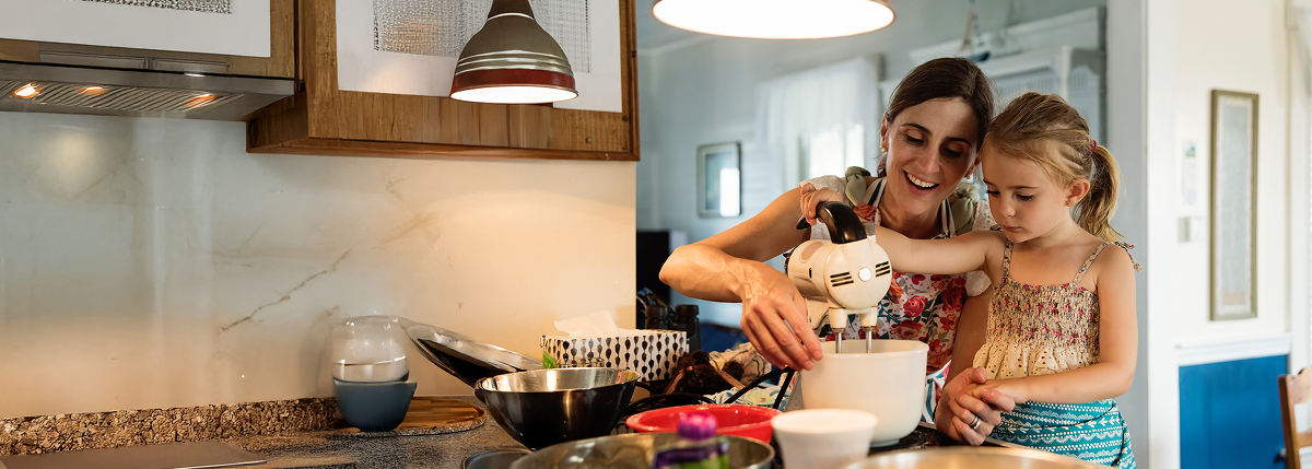 A mother and daughter in the kitchen mixing together ingredients in a bowl with a hand mixer