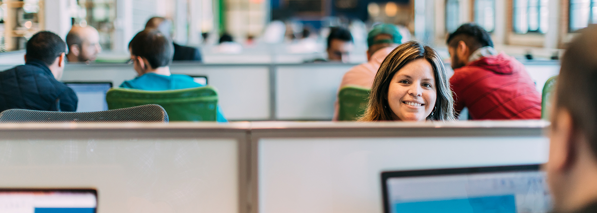 A woman sitting behind her work desk, looking straight on and smiling
